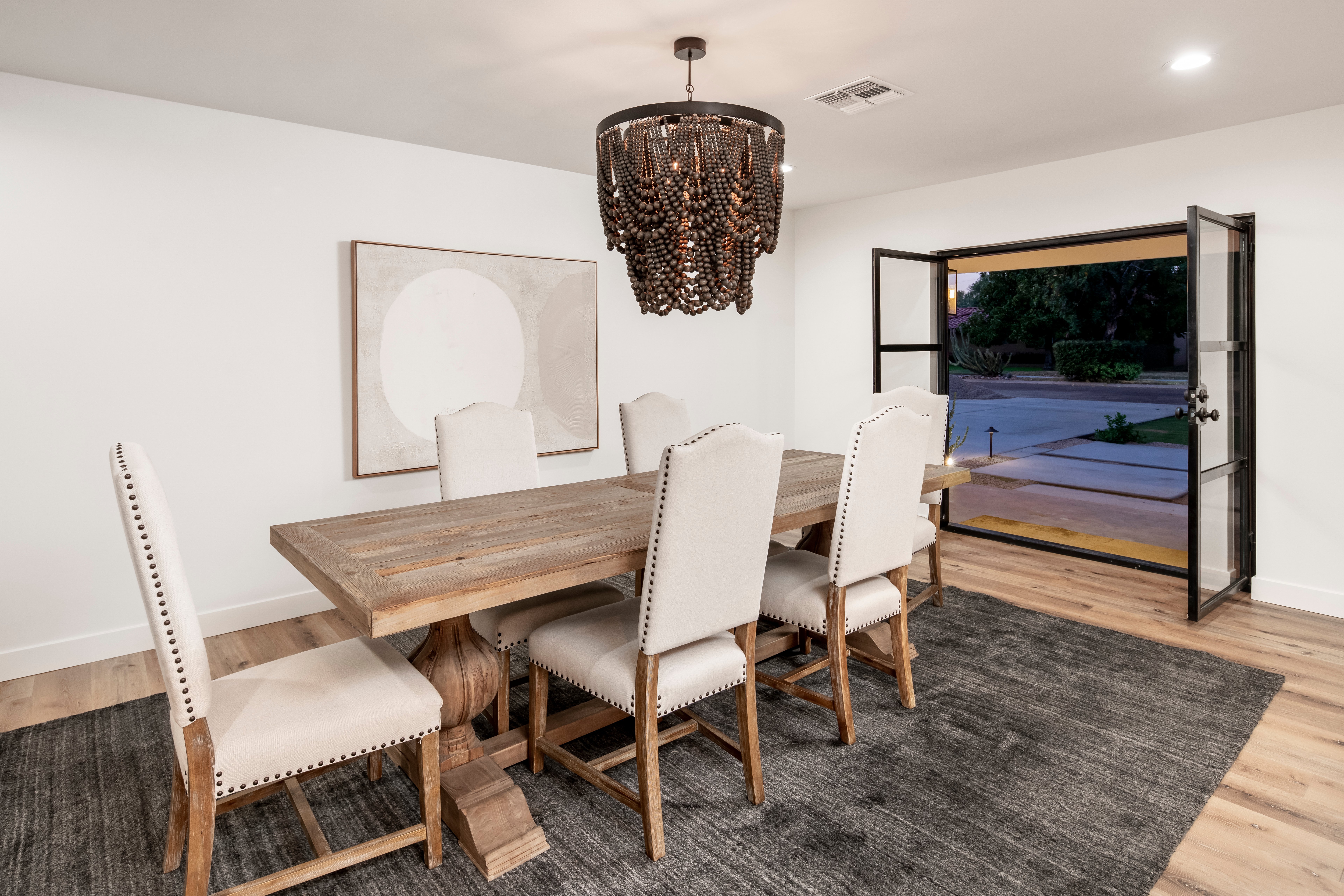 Elegant dining room decorated in whites and greys with a large wood table opens to the Arizona evening